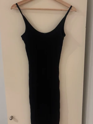 Svart ribbad långklänning Bik Bok - Säljer en svart ribbad långklänning från Bik Bok i storlek XS. Klänningen har smala axelband och är figurnära med stretchigt material. Enkel och stilren design som passar perfekt till många olika looks.