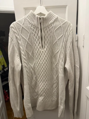 Vit stickad half zip tröja från Zalando  - Säljer en vit stickad tröja med half zip och hög krage. Tröjan har ett snyggt kabelstickat mönster med både rutor och flätor på framsidan. Ribbstickade muddar vid ärmslut och nederkant. Den är perfekt nu för vintern!