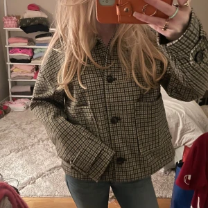 Rutig jacka från Nelly i ullmix - Säljer en snygg rutig jacka från Nelly i beige, svart och brunt. Jackan har stora knappar framtill, två rejäla fickor och klassisk krage. Materialet är en ullmix som känns både varm och trendig. Perfekt till jeans och boots för en cool look.