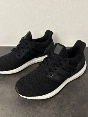 Svarta Adidas Ultraboost skor - Säljer ett par svarta Adidas Ultraboost sneakers med vit sula och klassiska tre ränder på sidan. De är helt oanvända, box följer med och pris är ganska fast på dessa!