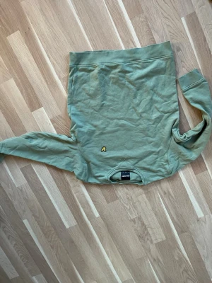Grön sweatshirt från Lyle & Scott - Säljer en grön sweatshirt från Lyle & Scott i storlek M. Tröjan har ett litet gult Lyle & Scott-logo broderat framtill och klassisk rund hals. Materialet är mjuk bomull och passformen är normal med långa ärmar och ribbade muddar.