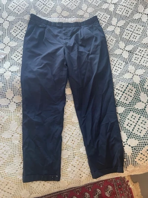 Mörkblå chinos/kostymbyxor med raka ben - Snygga mörkblå kostymbyxor/chinos med raka ben och klassisk passform. Byxorna har två framfickor med knappdetaljer och två bakfickor. Tillverkade i ett mjukt bomullsmaterial. Ingen lapp men skulle säga XL-2XL. Normalhöga i midjan och normallånga. Köpta på herravdelningen men har passat mig som kvinna också.