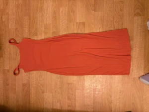 Ribbad orange långklänning - Säljer en ribbad långklänning i stark orange färg med smala axelband. Klänningen är figurnära. Perfekt för dig som gillar färg och vill sticka ut med en minimalistisk look.