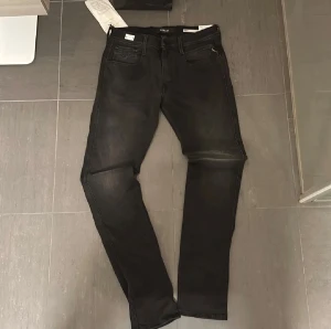 Replay Anbass svarta jeans - Svarta Replay Anbass jeans med slim passform och klassisk femficksdesign. Jeansen har svarta sömmar, Replay-logga på fickan och är tillverkade i stretchigt jeansmaterial för skön komfort. Snygg tvättad look och raka ben.