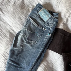 Blå jeans från Jacob Cohen, storlek 32 - Snygga blå jeans från Jacob Cohen i storlek 32. Jeansen har en klassisk femficksdesign, coola blå detaljer vid knappar och sömmar samt ett unikt mönstrat innerfoder med bilar. Materialet är mjukt jeans och passformen är normal med rak siluett.