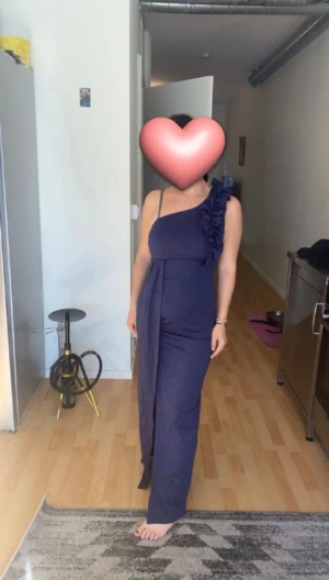 Marinblå oneshoulder långklänning - Säljer en marinblå långklänning med oneshoulder och volangdetalj på axeln. Klänningen har en elegant, figurnära passform och ett långt tygstycke som hänger ner från axeln. Perfekt för dig som vill sticka ut med en unik och stilren look.