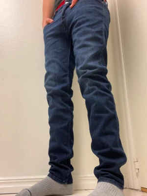 Replay Anbass mörkblå jeans - Snygga Replay Anbass jeans i mörkblå tvätt med klassisk femficksdesign och raka ben. Jeansen har silverfärgad knapp, tydliga sömmar och Replay-logga på myntfickan. Perfekta för dig som gillar stilrena och tidlösa jeans med modern passform.