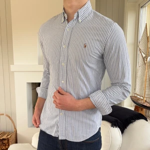Blårandig skjorta från Ralph Lauren slim fit - Snygg blårandig skjorta från Ralph Lauren i slim fit-modell. Skjortan har klassisk button-down krage, broderad logga på bröstet och vita knappar framtill. Tillverkad i mjuk bomull som känns skön mot huden. Perfekt för dig som gillar stilrena och fräscha plagg.