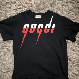 Gucci blade t-shirt  - Snygg svart t-shirt från Gucci med ett iögonfallande tryck i vitt och rött på framsidan. Tillverkad i mjuk bomull för en bekväm passform. Säljer pårgrund av att den var för stor. Perfekt till sommartider men även på våren under en fet tröja🖤❤️ T-shirten är som ny och priset är ej hugget i sten. Bara att höra av sig vid minsta fundering! Självklart är de äkta 