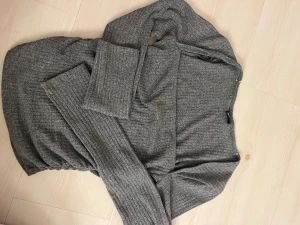 Grå ribbad stickad tröja - Snygg grå stickad tröja med ribbad struktur och lång ärm. Modellen är kroppsnära och har en enkel, stilren design som passar perfekt för dig som gillar en clean look. Mjuk och skön kvalitet som känns bekväm hela dagen.