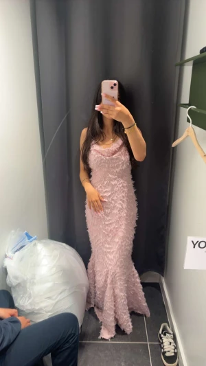 Ljusrosa långklänning från Vila - Säljer en maxiklänning från Vila i färgen Misty Rose. Klänningen har smala axelband,öppen rygg, figurnära passform och är täckt av fluffiga detaljer som ger en mysig textur. Perfekt för dig som vill sticka ut med en unik look.