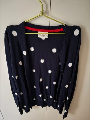 Mörkblå prickig kofta - Snygg mörkblå kofta från Holly & Whyte med vita prickar och knappar framtill. Köpte på Vinted men den är ganska ny, har aldrig använt. M men passar bra som S med. 
