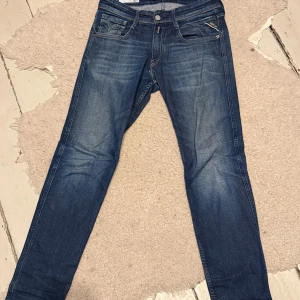 Replay Anbass slim fit jeans blå - Snygga blå Replay Anbass jeans i slim fit med klassisk femficksdesign och coola slitningar. Jeansen har raka ben, medelblå tvätt och detaljerade bakfickor med Replay-logga. Perfekt passform för dig som gillar en modern och stilren look.