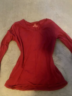 Vinröd långärmad v-ringad tröja  - Snygg vinröd långärmad tröja från Primark med v-ringad hals. Modellen är stretchig och sitter skönt mot kroppen. Perfekt för dig som gillar enkel stil med lite färg. Materialet är mjuk bomull som känns bekvämt hela dagen.