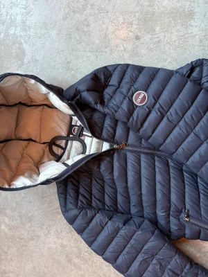 Mörkblå Colmar dunjacka med huva - Snygg mörkblå dunjacka från Colmar med huva och två dragkedjeförsedda fickor. Jackan har quiltad design och ljus insida. Perfekt för kallare dagar och den har en modern, slim passform.