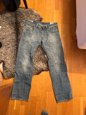 Diesel Larkee jeans blå, storlek 34 - Säljer ett par klassiska Diesel Larkee jeans i blå tvätt, storlek 34. Jeansen har raka ben, slitna detaljer och coola revor på framsidan. Materialet är robust denim med snyggt sliten look och patch på bakfickan. Perfekt för dig som gillar avslappnad stil. Raka jeans passar dig mellan 180-185.