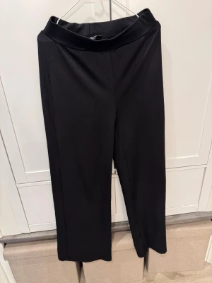 Svarta ribbade byxor från 157, M - Svarta ribbade byxor från 157 i storlek M. Byxorna har en bred resår i midjan och ett loose, wide fit med raka ben. Materialet är mjukt och stretchigt, perfekt för chill dagar. Snyggt ribbad struktur som ger en cool vibe.