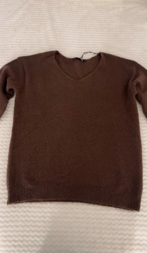 Brun stickad v-ringad tröja 157 - Mysig brun stickad tröja från 157 med v-ringad hals och långa ärmar. Tröjan har ribbade muddar vid ärmslut och nederkant, vilket ger en chill och enkel look. Perfekt för lager-på-lager under hösten och vintern.