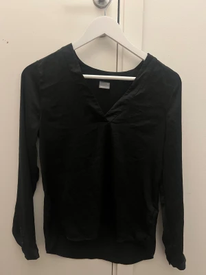 Svart blus från Gina tricot  - Säljer denna svarta blusen från Gina som är i nått tunt satin material, lite urringad. Perfekt för fest, skola, jobb, alla tillfällen! ❤️