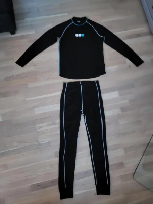 Svarta underställ  från True North - Svart underställ från True North med smal passform och ljusblå kontrastsömmar längs benen. Materialet är syntet och designen är enkel med muddar vid bensluten. Perfekt för kalla dagar och träning utomhus.