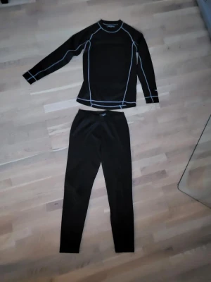 Svart underställ Stormy Weather - Svart underställ från Stormy Weather i storlek S. Tröjan har kontrasterande vita sömmar och är gjord i ett syntetmaterial som andas, perfekt för sport eller utomhusaktiviteter. Slimmad passform och stilren design.