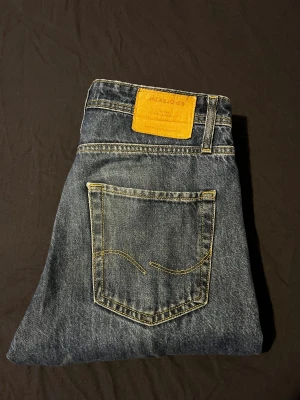 Jack & Jones Relaxed Chris jeans blå - Snygga blå jeans från Jack & Jones, modell Relaxed Chris. Klassisk femficksdesign med kontrastsydda sömmar och brunt läderpatch bak. Rak passform med normal midja, tillverkade i slitstarkt bomullsjeansmaterial. Perfekt för dig som gillar avslappnad stil. Hör av er vid frågor!