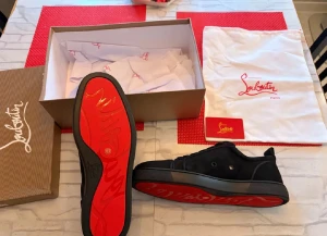 Svarta sneakers från Louboutin äkta - Säljer ett par svarta sneakers från Louboutin med ikonisk röd sula och diskret logga. Skorna har rund tå, platt sula och är tillverkade i skinn med snygga detaljer. Perfekt för dig som gillar exklusiv streetstyle och vill sticka ut med en lyxig touch. Finns äkthetsbevis