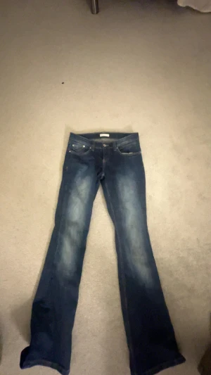 Blå bootcut jeans från Perfect Jeans - Snygga blå bootcut jeans från Perfect Jeans i storlek 38. Klassisk femficksmodell med ljusare tvättade partier på benen och kontrastsömmar på bakfickorna. Jeansen har låg midja och är tillverkade i jeansmaterial med stretch för skön passform.