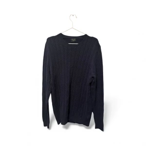 Mörkblå stickad tröja Massimo Dutti - Snygg mörkblå stickad tröja från Massimo Dutti i storlek L. Tröjan har ett diskret mönster med sicksackstruktur och är tillverkad i bomull och silke. Rund hals och långa ärmar ger en klassisk och stilren look. Perfekt för dig som gillar enkel men sofistikerad stil.