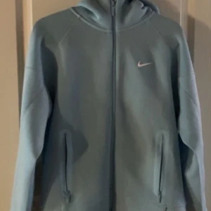  Nike Nocta Hoodie - Säljer en ljusblå Nike NOCTA hoodie med hel dragkedja framtill och huva. Tröjan har två fickor med dragkedja och diskret Nike-logga på bröstet. NOCTA-tryck på ärmen och detaljer bak. Perfekt för chill eller streetwear.