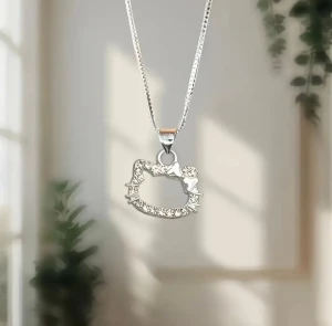 Hello Kitty halsband i silver - Snyggt halsband med en silverfärgad kedja och ett hänge i form av Hello Kittys ansikte. Hänget har en glittrig yta och en liten rosett på sidan, vilket ger en söt och lekfull touch. Perfekt för dig som gillar kawaii och vill sticka ut. Längd: 40+5 cm