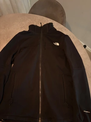 Svart vindjacka från The North Face - Svart vindjacka från The North Face med hög krage och hel dragkedja framtill. Jackan har två sidofickor med dragkedja och en bröstficka. Materialet är slitstark polyester och Windwall-teknologi för extra vindskydd. 