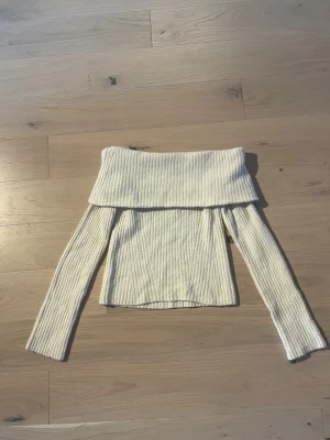 Stickad tröja - Jag säljer en offshoulder ribbad tröja från H&M i storlek XS. Tröjan är krämvit, har lång ärm och är stickad i ett mjukt material. Den breda kragen ger en snygg offshoulder-look och den ribbade strukturen gör den extra cozy. Perfekt för dig som gillar stilrena vibes. Den har en liten blå fläck på på baksidan av armen men det märks inte. (Kolla på bilden)
