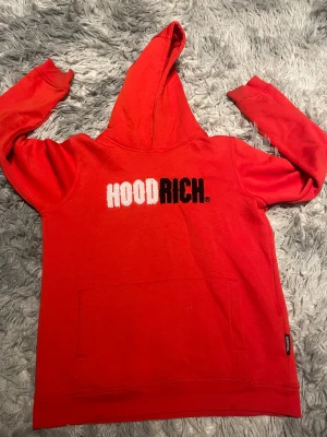 Röd HOODRICH hoodie XL - Snygg röd hoodie från HOODRICH i storlek XL med broderad logga i vitt och svart på bröstet. Tröjan har huva, lång ärm och en stor magficka framtill. Perfekt för dig som gillar streetwear och vill sticka ut med en fet logga.