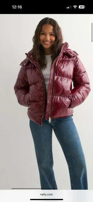 Vinröd pufferjacka med huva - Säljer en vinröd pufferjacka från Nelly med glansig finish och huva. Jackan har dragkedja framtill och är quiltad för extra värme. Passformen är normal och jackan har långa ärmar. Perfekt för kalla dagar när du vill vara både varm och snygg.