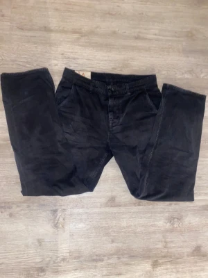 Svarta jeans från Nudie Jeans W31 L32 - Svarta jeans från Nudie Jeans i klassisk rak modell. Byxorna har fem fickor, knapp och dragkedja framtill samt subtila sömmar. Materialet är slitstarkt jeans och färgen är mörk svart, perfekt för en clean och stilren look. Modellen är lazy Leo. Vid snabb affär 299kr annars 349kr!