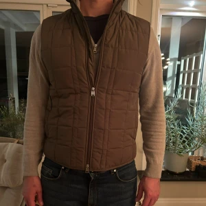 Brun quiltad dunväst Tiger of Sweden - Säljer en brun quiltad dunväst från Tiger of Sweden. Västen har hög krage, raka linjer och dragkedja framtill. Den är lätt vadderad och har ett stilrent rutmönster. Perfekt för lager-på-lager och funkar till både jeans och hoodie.