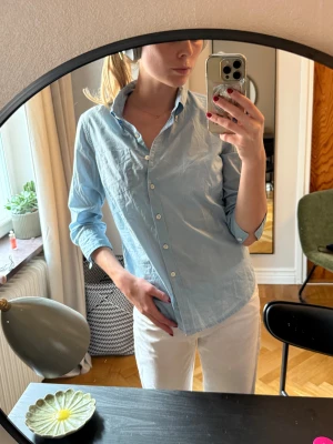 Ljusblå skjorta Ralph Lauren - Klassisk ljusblå skjorta från Ralph Lauren i bomull. Skjortan har knappar hela vägen, bröstficka och en snygg krage. Perfekt passform med långa ärmar och stilren look..