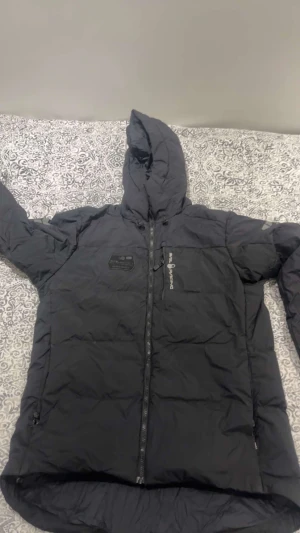 Svart vinterjacka från Sail racing  - Svart vinterjacka Sail racing med huva och hel dragkedja framtill. Jackan har en quiltad design och två sidofickor med dragkedja. Perfekt för kalla dagar och har en clean look med diskreta logodetaljer på bröstet och ärmen.