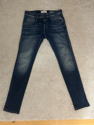 Replay Anbass mörkblå jeans skinny - Snygga Replay Anbass jeans i mörkblå tvätt med skinny passform. Klassisk femficksdesign, bruna detaljer på bakfickan och lätt slitna partier för en cool look. Perfekt för dig som gillar smalare jeans med modern stil och dom är minimalt