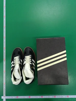Adidas Samba svartvita sneakers - Adidas Samba sneakers i svart och vitt med klassiska tre ränder på sidan, vit plös och häl samt gummisula. Ovandelen är i mocka och skinn med snörning och gulddetaljer vid snörhålen. Snygg retrostil och låg profil, perfekt för dig som gillar streetwear.