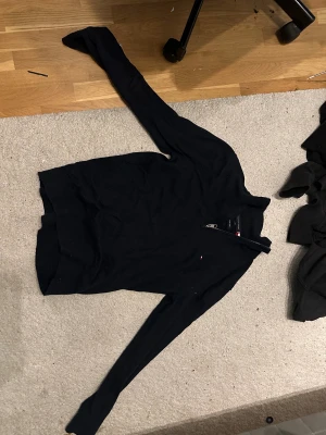  Tommy Hilfiger quarterzip - Svart långärmad tröja från Tommy Hilfiger med half zip-dragkedja vid halsen och diskret logga på bröstet. Tröjan har en klassisk passform och är gjord i mjukt bomullsmaterial, perfekt för chill dagar eller när du vill vara lite extra snygg.
