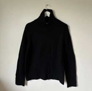 Svart polotröja i ull från Arket - Svart ribbstickad polotröja från Arket i storlek S. Tröjan har en hög krage och är tillverkad i mjuk ull enligt Responsible Wool Standard. Perfekt för dig som gillar minimalistisk stil och vill ha något varmt och snyggt till höst och vinter. 4Ö14