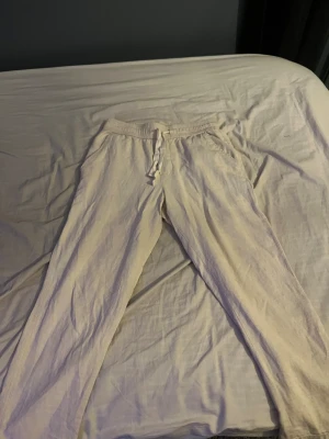 Beige linnebyxor från Zara med snörning - Snygga beige linnebyxor från Zara med elastisk midja och snörning framtill. Byxorna har raka ben och sidofickor, perfekta för en chill och avslappnad stil. Luftigt material som passar bra när det är varmt ute.