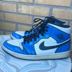 Nike Air Jordan 1 Mid SE ’Signal Blue’ - Säljer ett par Air Jordan 1 Mid SE “Signal Blue”  i storlek 44. Skorna har en riktigt snygg färgkombination i blått, vitt och svart med glansigt patentläder som sticker ut.  Äkta vara – Nike / Jordan Brand Perfekta sneakers för både streetwear och samlare. Nypris: 3299:-