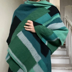 Varm sjal i gröna toner - Stor och mjuk styckad sjal (sannolikt ullblandning) med rektangulär form. Mysig att svepa runt sig för extra värme och stil. Kan också användas som halsduk eller snygg som mindre filt i soffan hemma eller på utflykten. Ett par pyttesmå hål-lagningar som inte syns. Färgerna kombineras snyggt med t ex  jeans, grå/beige, mörkblå eller bruna toner. TIPS! Perfekta gåvan till någon som behöver lite extra värme med många kombinationsmöjligheter. 