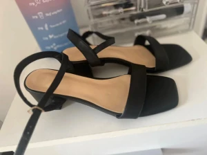 Svarta sandaler med låg klack, strl 38 - Snygga svarta sandaler med breda remmar och fyrkantig tå. De har en låg blockklack och justerbart spänne runt ankeln. 38 