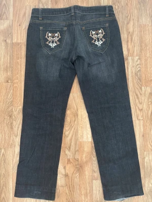 Svarta jeans med broderade fickor från Mexx - Snygga svarta jeans från Mexx i storlek 40 med coolt broderi på bakfickorna. Klassisk femficksmodell med orangea sömmar och knapp med Mexx-logga. Jeansen har rak passform och är tillverkade i slitstarkt denimtyg.