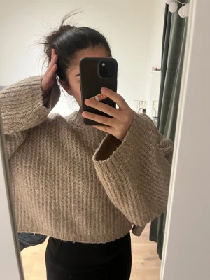 Beige stickad - Säljer en beige croppad stickad tröja med breda ärmar och ribbad struktur. Tröjan har en loose passform och rund halsringning, perfekt för lager-på-lager under hösten och vintern.