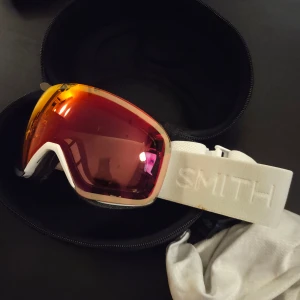 Smith I/O Mag skidglasögon röd/vit - Säljer ett par Smith I/O Mag skidglasögon med röd/orange spegellins och vit ram. Elastiskt vitt band med Smith-logga. Linsen är Photo Chromapop och ger grym kontrast i snön. Sitter bekvämt och passar perfekt för vinterns äventyr. Helt nya! Aldrig använda 